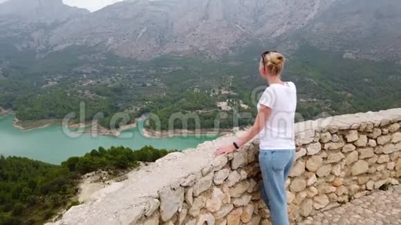 一个年轻的女人从一座古老城堡的墙上看到一个美丽的风景有一个蓝色的湖和山视频的预览图
