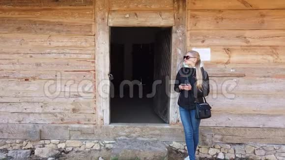 在一个老村庄的木屋附近使用智能手机的女人视频的预览图