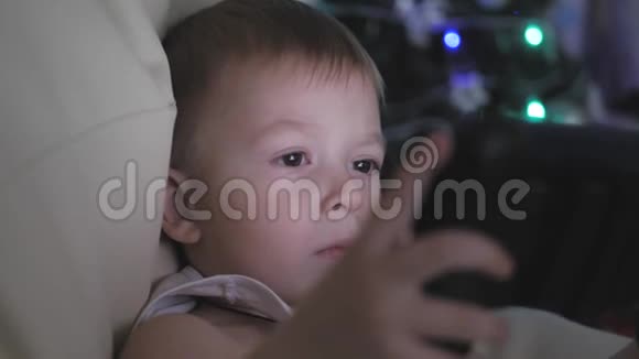快乐的小男孩玩看看平板电脑附近的圣诞树在内部的家夜晚的圣诞节视频的预览图