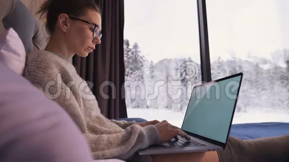一幅有魅力的自由职业者的画像她戴着眼镜穿着一件毛衣穿着长袜坐在生态屋的床上视频的预览图