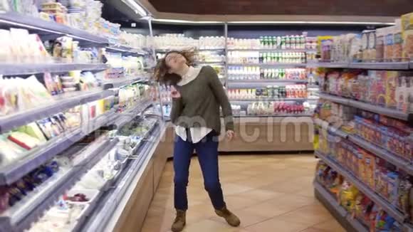 穿着牛仔裤和毛衣的年轻女子站在杂货店过道上跳舞的完整镜头视频的预览图