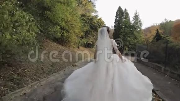 美丽可爱的新娘穿着婚纱在公园里奔跑慢动作视频的预览图