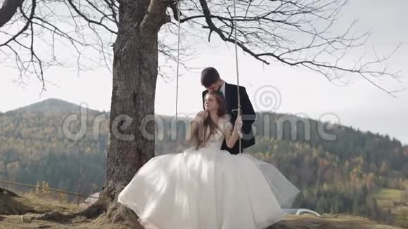 新婚夫妇白种人新郎和新娘在山坡上骑着一条秋千视频的预览图
