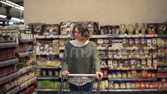 一个留着波浪发的女人的肖像穿着休闲装开着购物车穿过满是商品的货架视频的预览图