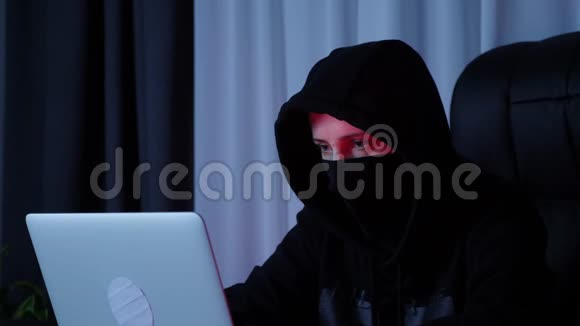戴着黑色面具和帽衫的女性脸看着笔记本电脑屏幕黑色引擎盖上的黑客脸看着电脑和打字代码Woma视频的预览图