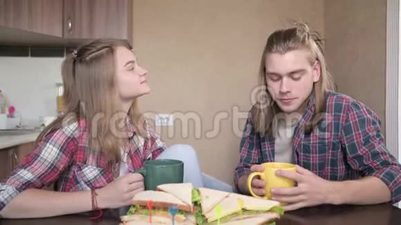 年轻夫妇坐在厨房里从杯子里喝酒聊天特写视频的预览图