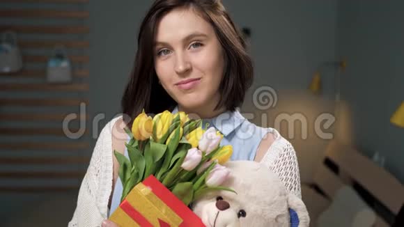 女孩带着礼物迷人的年轻女子独自在房间里手里拿着一束黄色郁金香手里拿着柔软的玩具视频的预览图