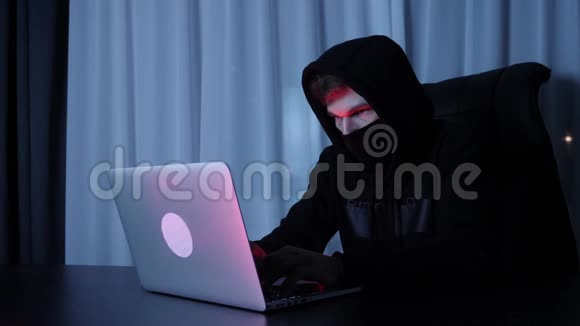 自信的男性黑客看着笔记本电脑屏幕戴着黑色面具和头巾的人坐在黑暗的房间里黑客攻击了网络社会安全视频的预览图
