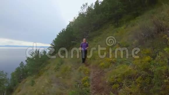 一个背着背包的女孩沿着海边陡峭的山坡上的小径奔跑视频的预览图