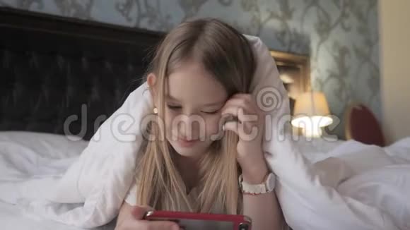 十几岁的女孩在床上玩社交网络上的平板电脑视频的预览图