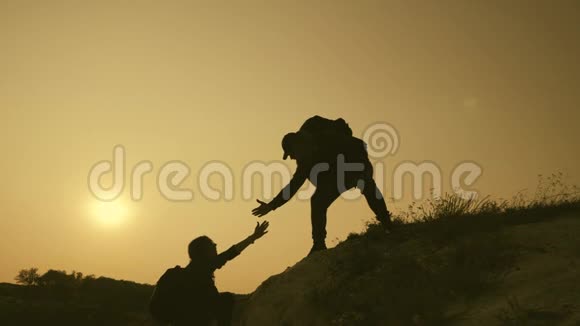 在两个登山者之间帮忙的剪影在山顶上有两个徒步旅行者一个男人帮助一个女人爬上一个纯粹的地方视频的预览图