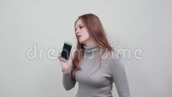 穿着灰色毛衣的红头发女人正在用手机或智能手机说话视频的预览图