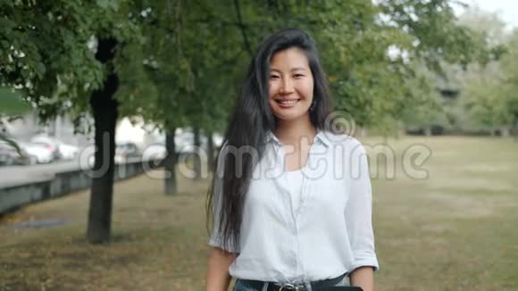 亚洲女孩在城市公园户外微笑的慢镜头肖像视频的预览图