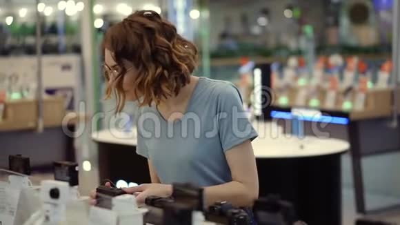 戴眼镜的年轻卷发女士在电子商店买了一台新的光电相机努力决定最好的模特视频的预览图