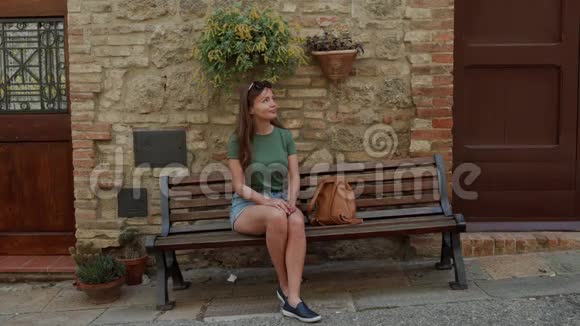 可爱的年轻旅游女孩坐在靠近旧砖墙和花盆的木凳上视频的预览图