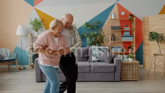 微笑的老太太和男人在家跳舞手牵手在室内欣赏音乐视频的预览图