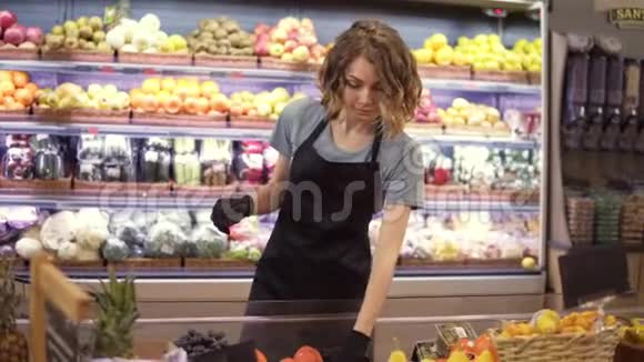 女店员戴手套和黑色围裙装满水果和蔬菜储藏架的画像视频的预览图