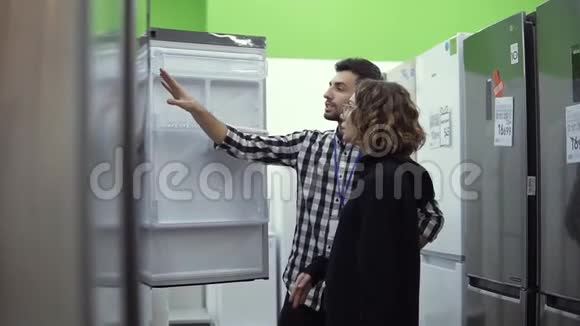 年轻女子站在冰箱的开门前与男性顾问讨论设计和质量问题视频的预览图