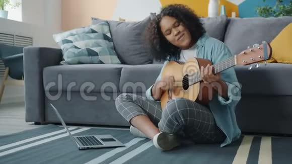 美国黑人女孩在家里弹吉他和使用笔记本电脑的肖像视频的预览图