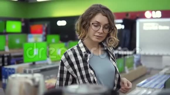年轻开朗积极向上的女性穿着格子衬衫戴着眼镜在家电商店里选择电子水壶视频的预览图