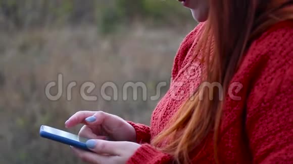 女孩的手拿着智能手机一个穿红色毛衣的年轻女孩站在街上时用电话视频的预览图