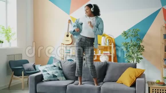 非洲裔美国女孩戴着耳机在沙发上跳舞听着音乐玩得开心视频的预览图