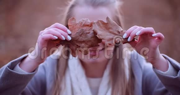 微笑的女人用秋天的树叶遮住眼睛视频的预览图