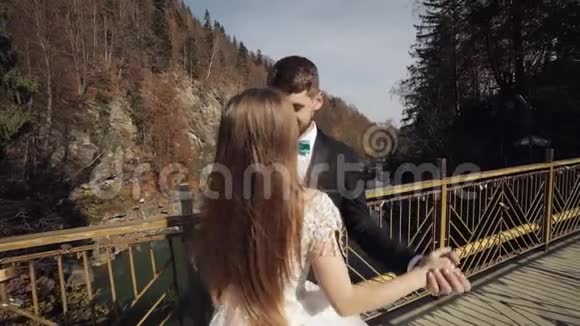 新婚夫妇白种人新郎和新娘在一山河上的桥上跳舞视频的预览图