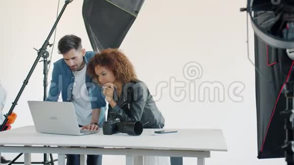 摄影师和模特在工作室里看笔记本电脑上的照片视频的预览图