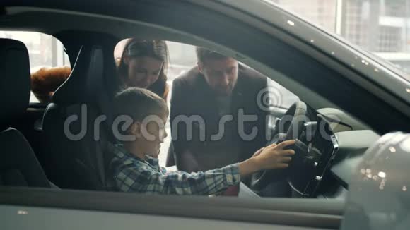 快乐的孩子坐在新车里拿着方向盘父母买汽车视频的预览图