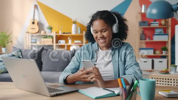 令人愉快的非裔美国女士触摸智能手机屏幕听耳机中的音乐视频的预览图