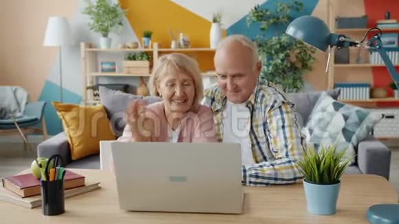 快乐的老年人使用笔记本电脑打视频电话在室内打手势视频的预览图