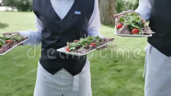 提供餐饮服务的两名服务员手里拿着西红柿沙拉米香肠肉菜庆祝婚礼或活动缓慢视频的预览图