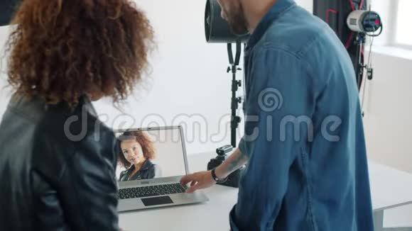 模特看着新照片和摄影棚里的摄影师交谈看着笔记本电脑屏幕视频的预览图