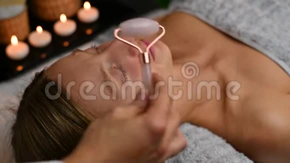 美容师用玉辊做专业面部按摩在水疗中心接受面部按摩的妇女视频的预览图