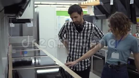 深色头发微笑的男人穿着格子衬衫戴着耳机选择了一个新的现代厨师顶在商店里他打算买视频的预览图