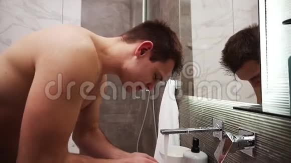从水龙头里冒出来的冷水下无顶的帅哥在水槽里洗脸肌肉男做晨间清洁视频的预览图