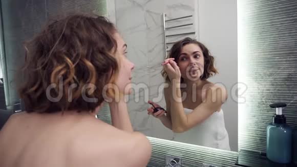 微笑的女人用眉毛阴影在镜子前化妆快乐的女性使用美容化妆品来提高自己视频的预览图