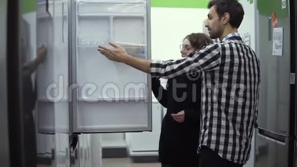 年轻夫妇在购买消费电子产品商店前先检查开门冰箱设计和质量视频的预览图