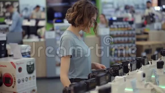 戴眼镜的年轻女子在电子商店买了一台新的光电相机试图决定最好的模式有过视频的预览图