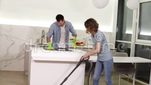 清洁日年轻夫妇打扫他们的公寓戴手套的男人擦拭厨房炉子女孩用清洁地板视频的预览图