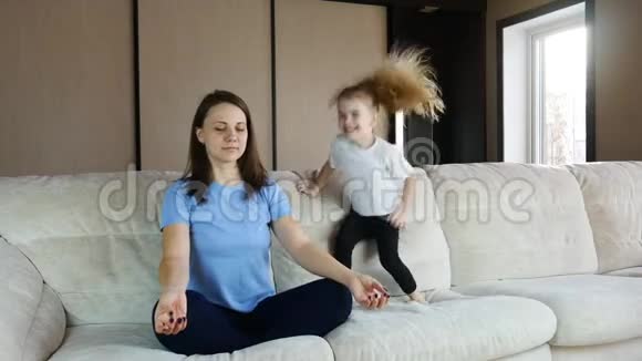 母亲坐在沙发上沉思活泼的孩子女儿在跳跃玩耍视频的预览图