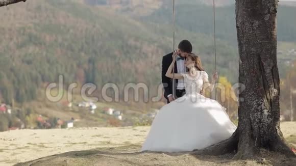 新婚夫妇白种人新郎和新娘在山坡上骑着一条秋千视频的预览图