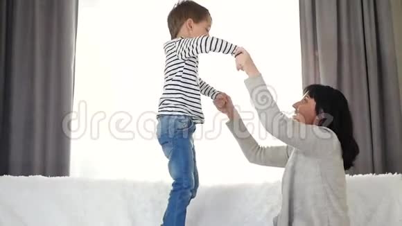 快乐开朗的男孩抱着妈妈的手跳在床上保姆妈妈在玩孩子情感视频的预览图