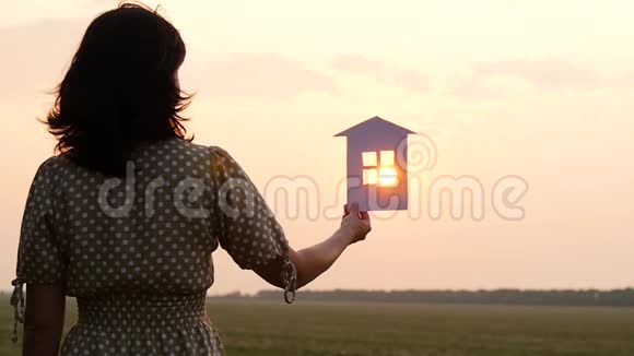 女孩手里拿着纸房子的模型日落时太阳的光芒穿过太阳的窗户视频的预览图