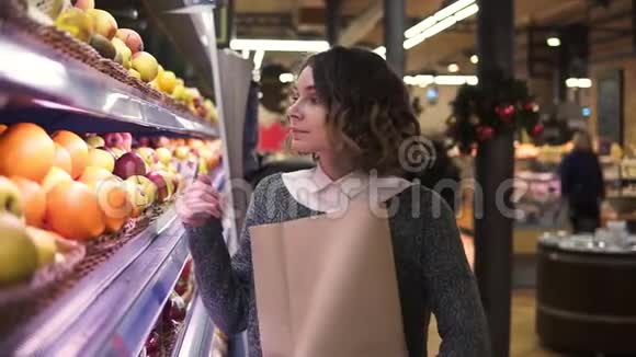 可爱的女孩在市场上买新鲜橘子美丽的年轻女子站在架子前面把橘子放到一个视频的预览图