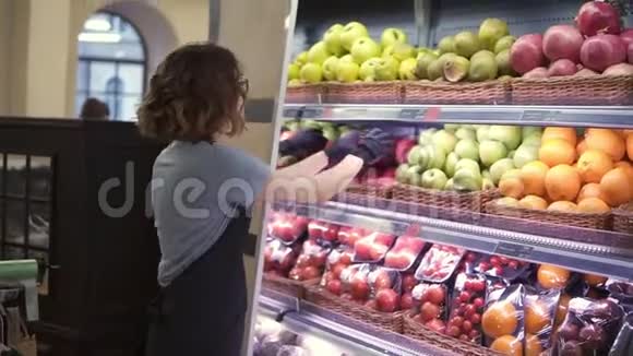 把穿着黑色围裙和手套的漂亮白种人工人关起来在超市里放水果青年雇员视频的预览图