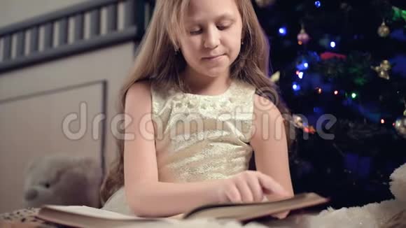 一个身穿节日礼服手里拿着一本书的金发小女孩坐在软玩具旁边背景是一个视频的预览图