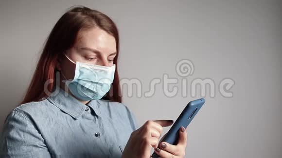 戴着医用口罩的年轻女性看着智能手机上的新闻视频的预览图