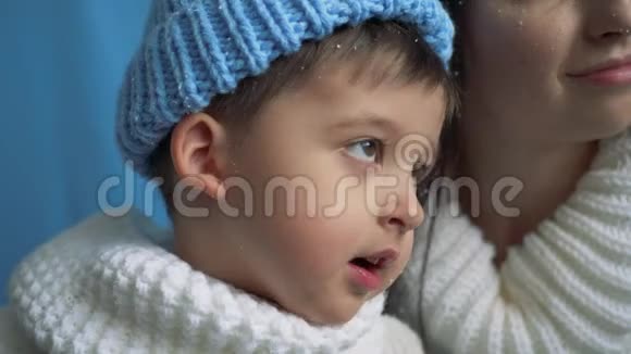 母亲和儿子穿着蓝色针织暖和帽子穿着白色毛衣在雪地里视频的预览图